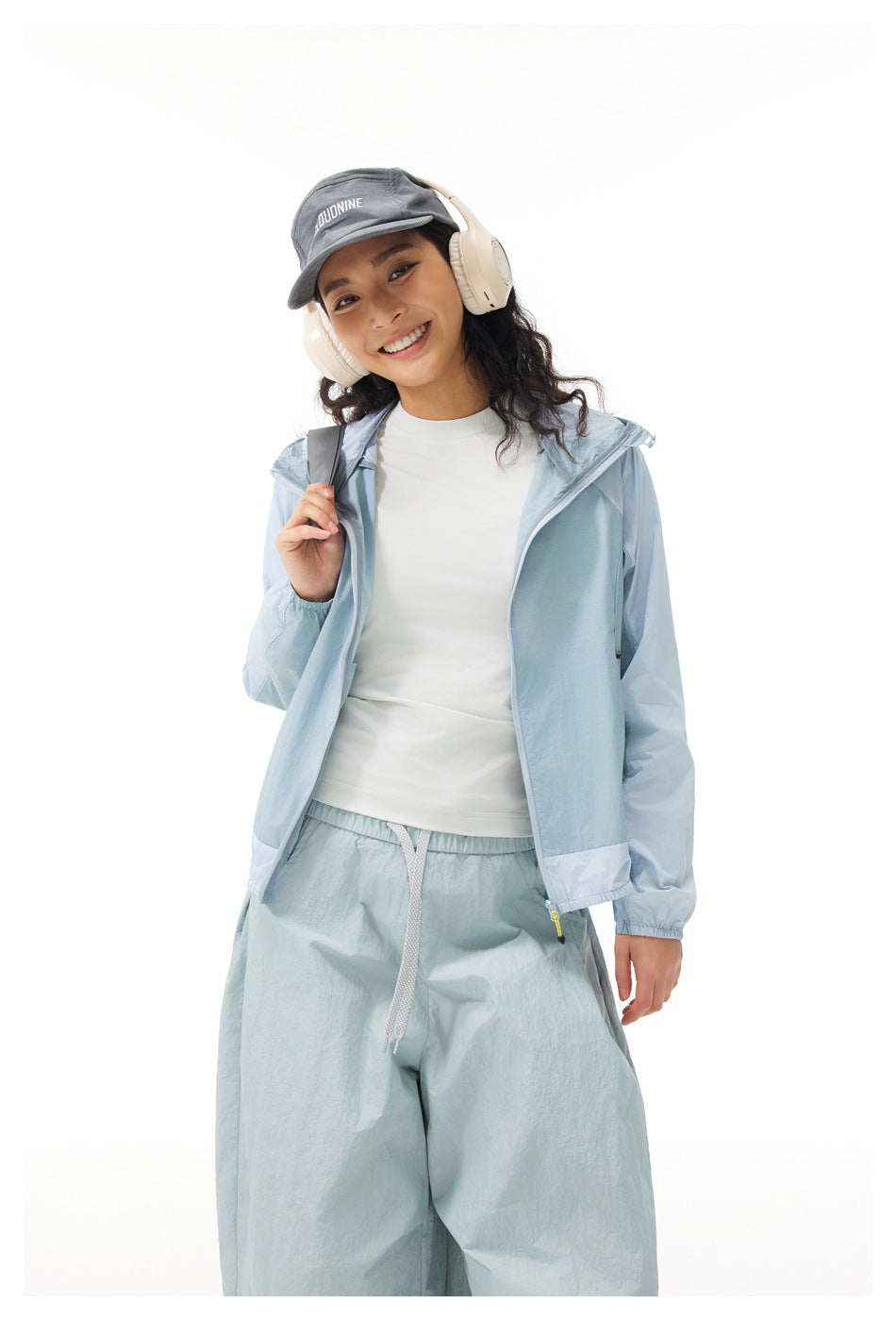 Model wearing an open light blue hooded jacket, white top, and loose pale blue drawstring pants.