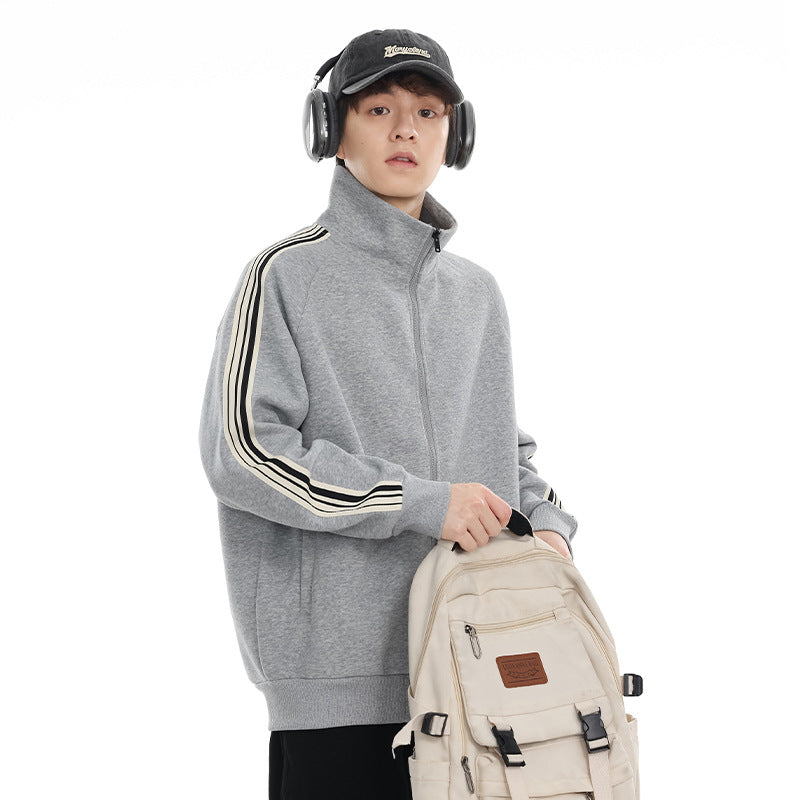 Model wearing a gray stand-collar zip jacket with dark triple sleeve stripes; a cream backpack partly covers it.