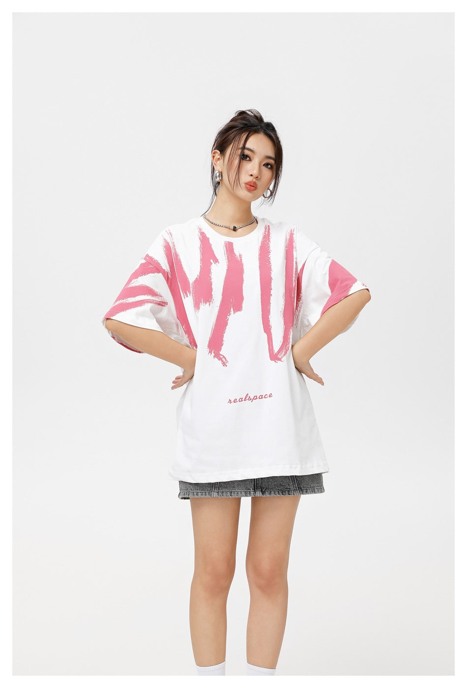 Model wearing white oversized T-shirt with pink brushstroke print, hands on hips, with a gray denim mini skirt