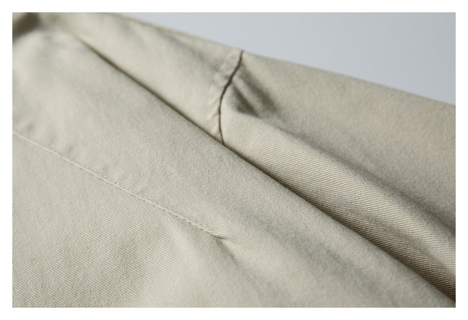 Close-up of light beige jacket fabric showing a folded seam and stitching.