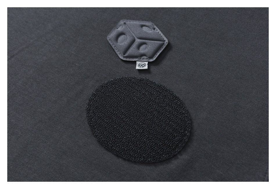 Close-up of dark charcoal fabric with a black oval patch, a small hexagonal tab, and a tiny label.
