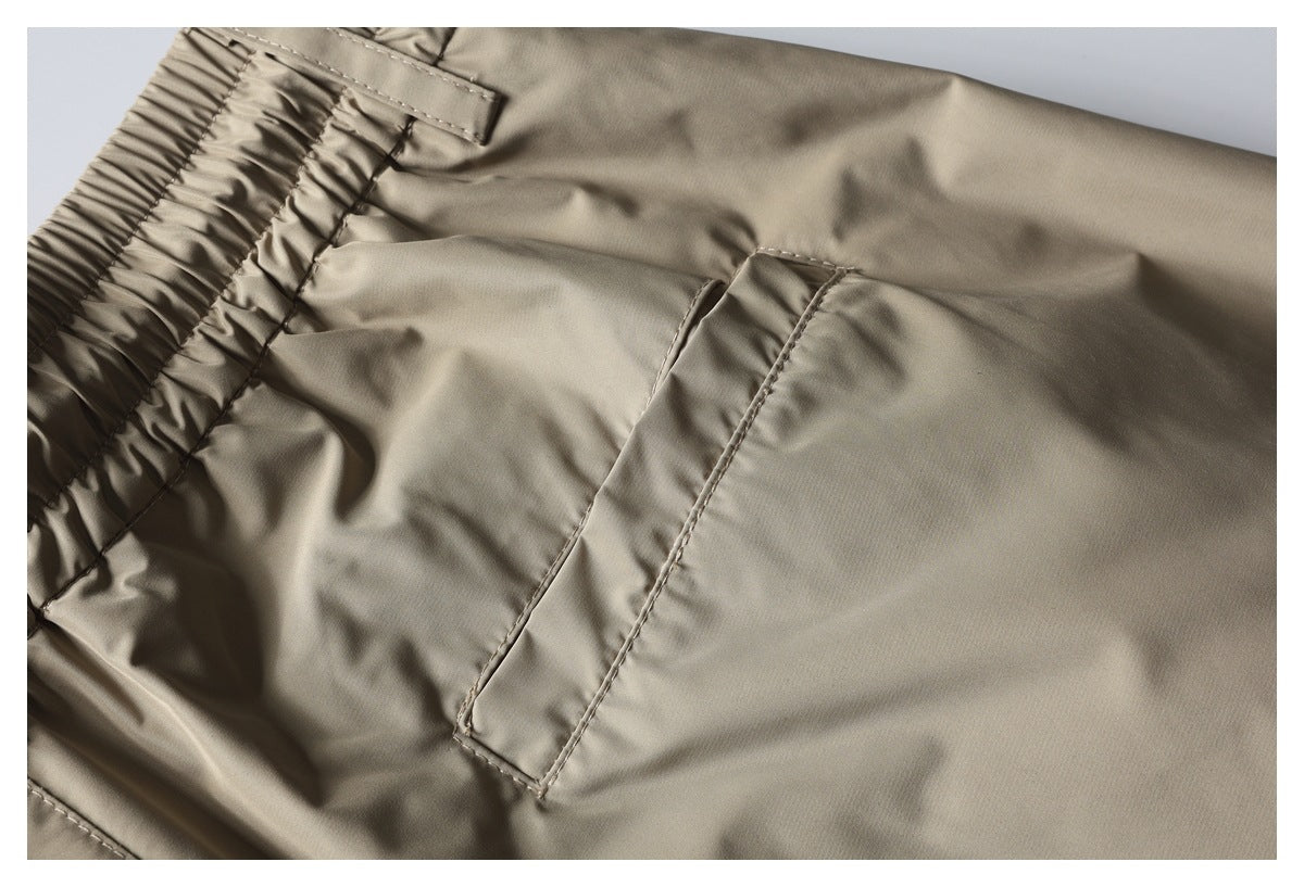 Close-up of taupe trousers showing the gathered elastic waistband and a slanted pocket.