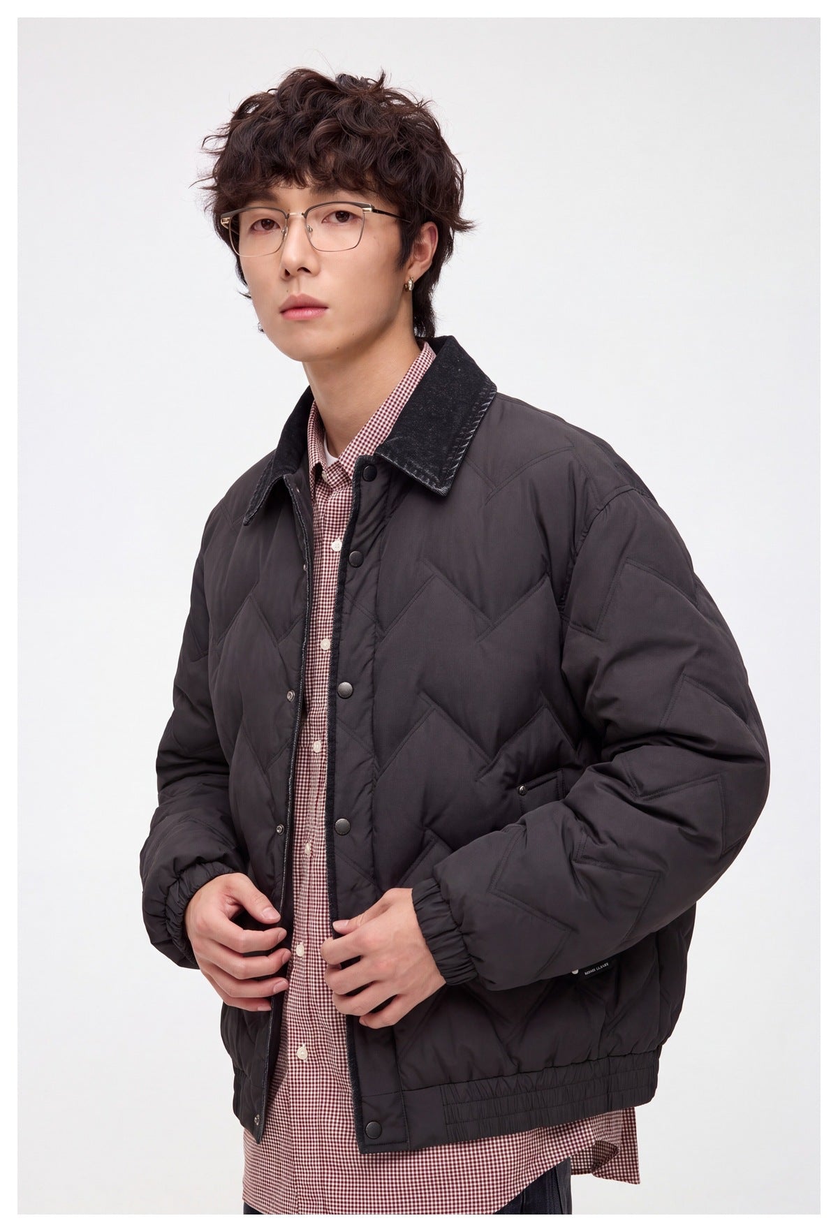 Close view of a model wearing a dark chevron-quilted jacket with a contrast collar, snap closure, and pockets.