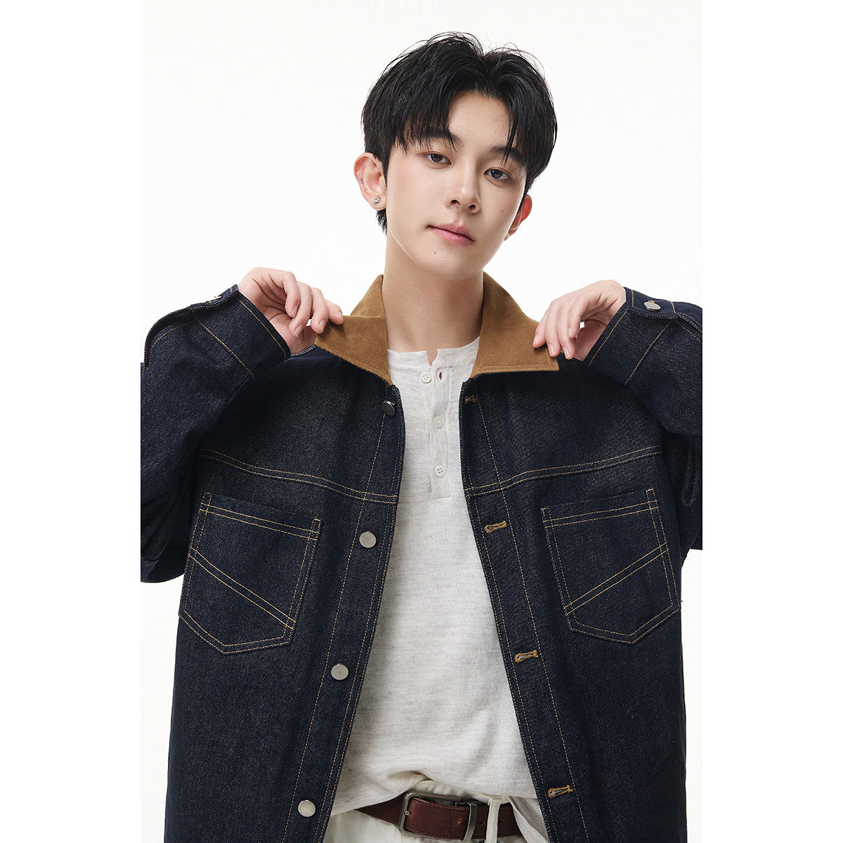 Close view of a model wearing an open indigo denim jacket with a tan collar, contrast stitching and two front pockets.