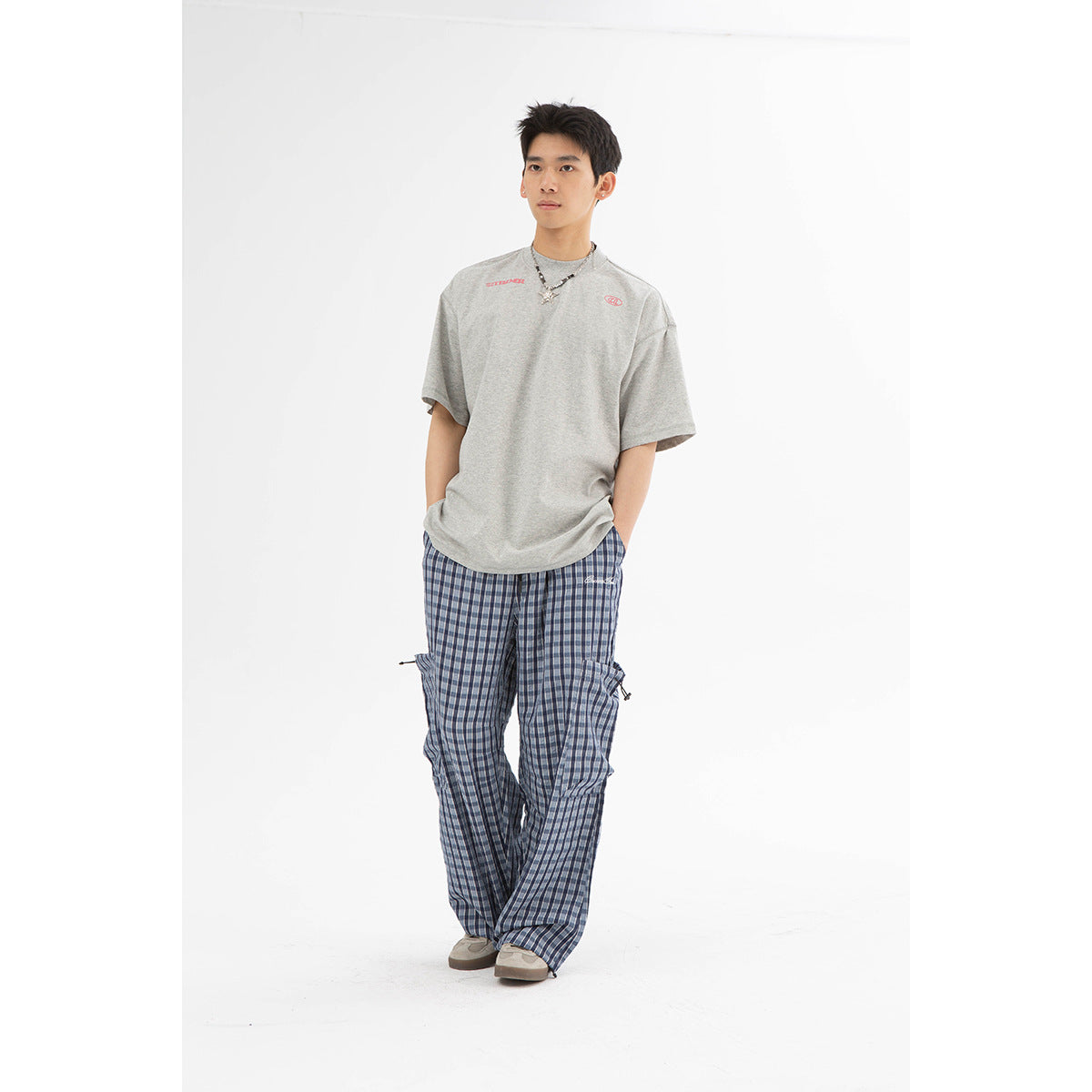 Full-length model wearing loose blue plaid cargo pants with side cargo pockets and a gray T-shirt.