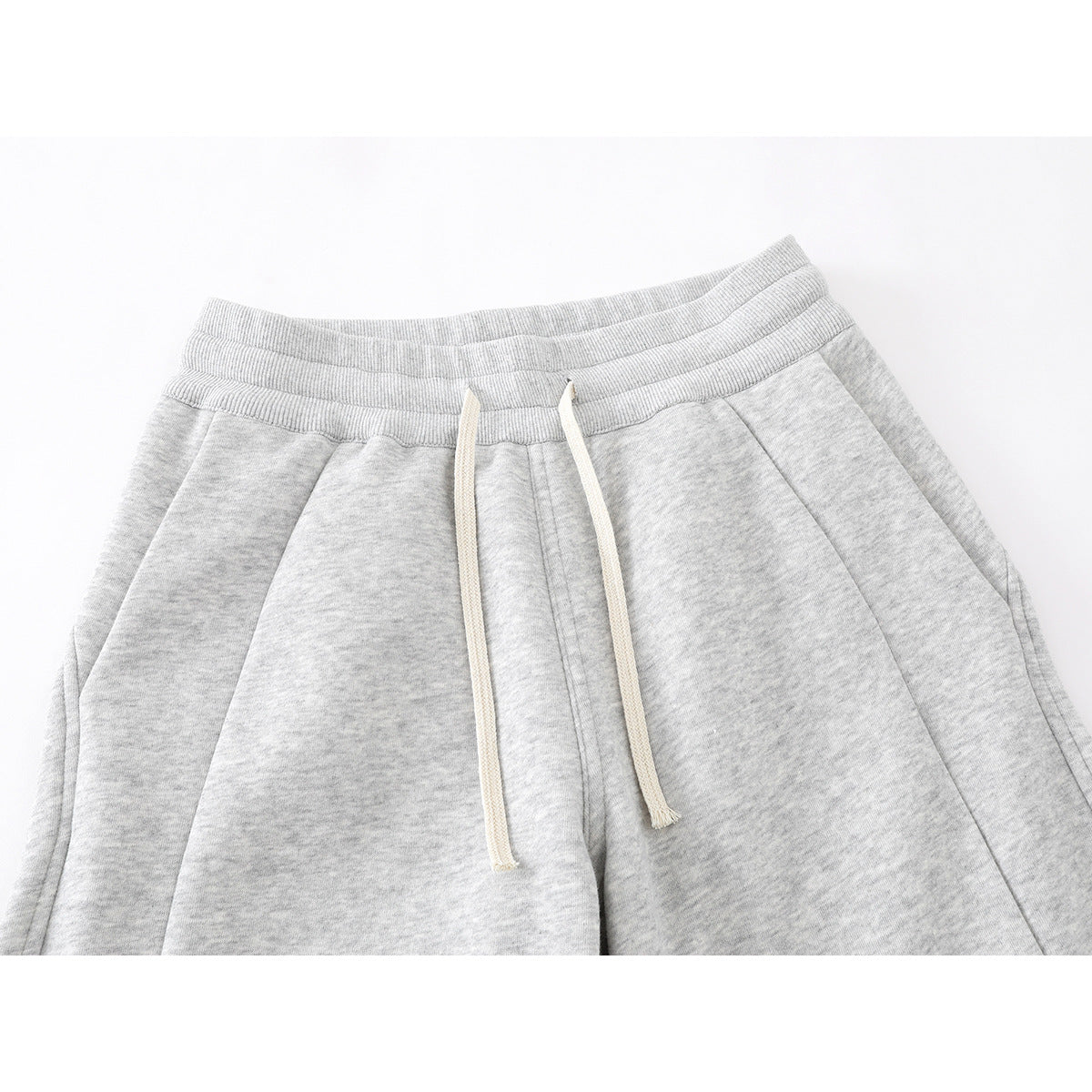 Close-up of light gray sweatpants showing the elastic waistband, white drawstrings, and front seams.