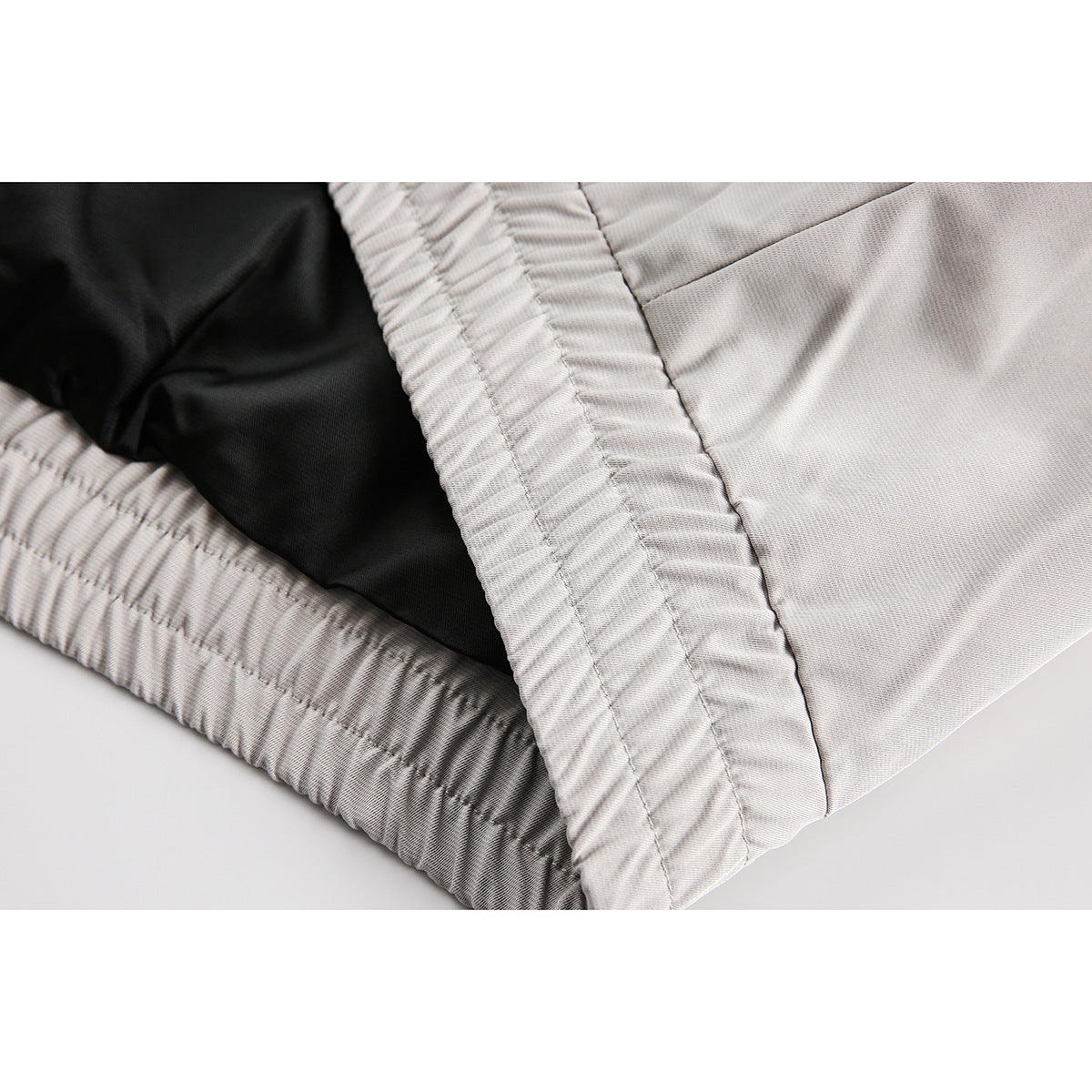Close-up of the light gray jacket's gathered inner hem, stitching, and black lining.