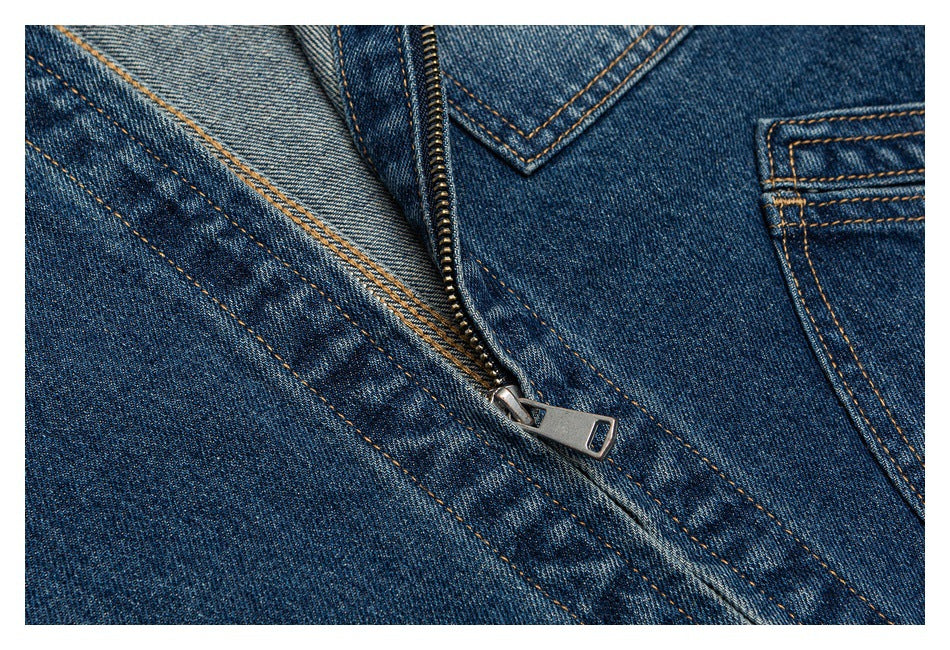 Close-up of dark blue denim with a metal zipper, orange stitching, and a pocket edge.