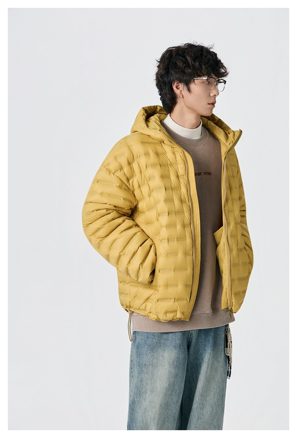 Three-quarter view of a model wearing an open mustard-yellow hooded quilted jacket over a taupe sweatshirt.