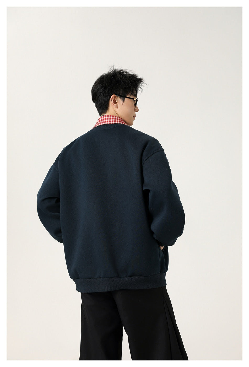 Rear view of a model wearing a dark navy jacket with a red checked collar and black trousers.