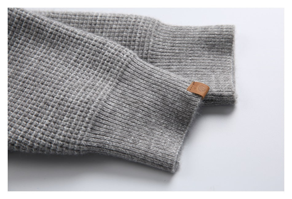 Close-up of a gray cardigan sleeve with a ribbed cuff and small leather tab.