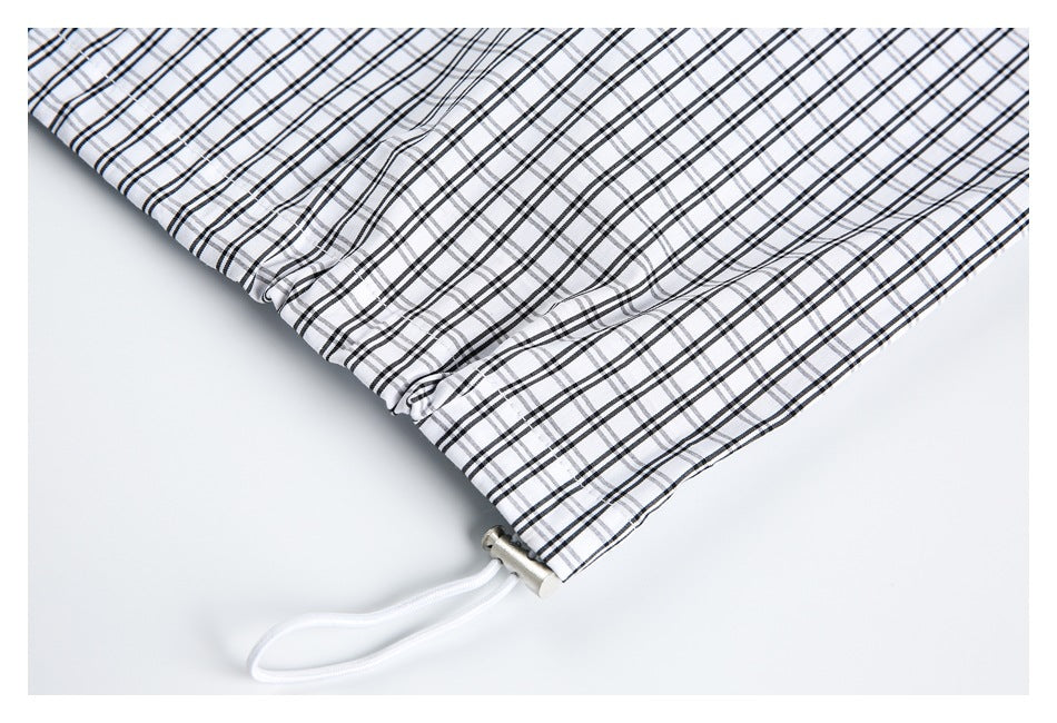 Close-up of a white drawcord and metal toggle at the hem of black-and-gray plaid fabric.