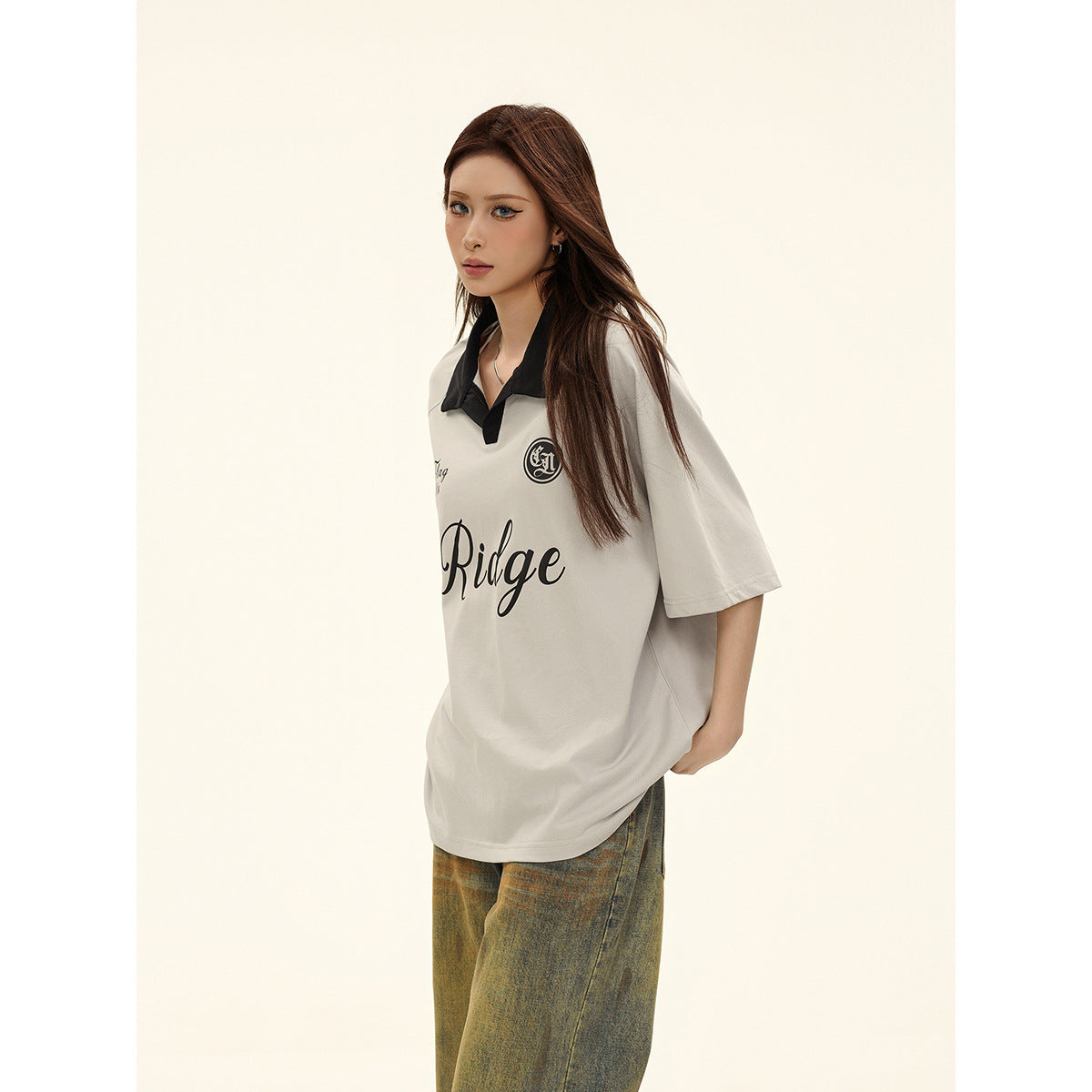 Closer angled view of a model wearing a light gray oversized polo with black collar and lettering.