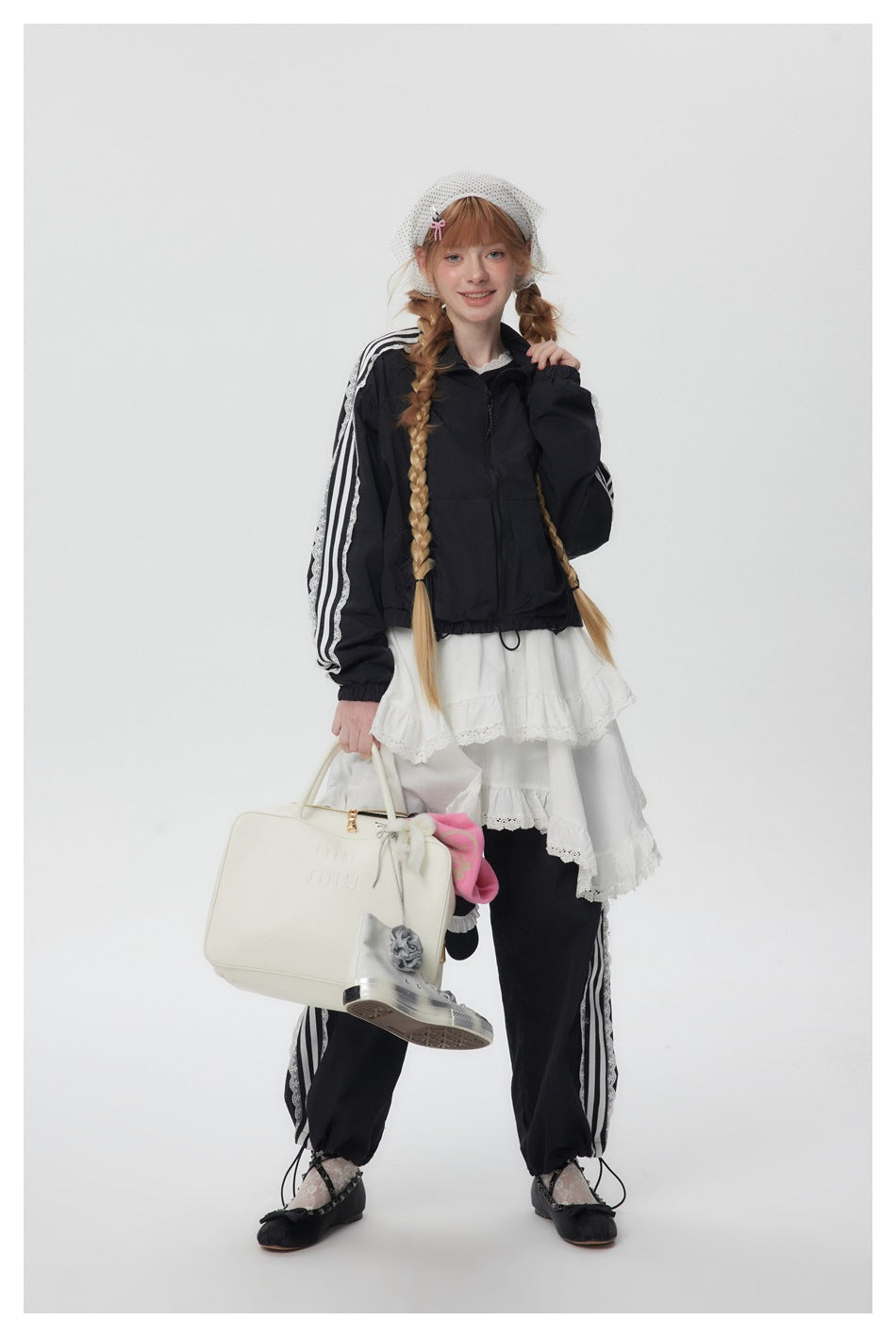 Full-length model wearing a black striped jacket, white tiered lace skirt, and matching black track pants.