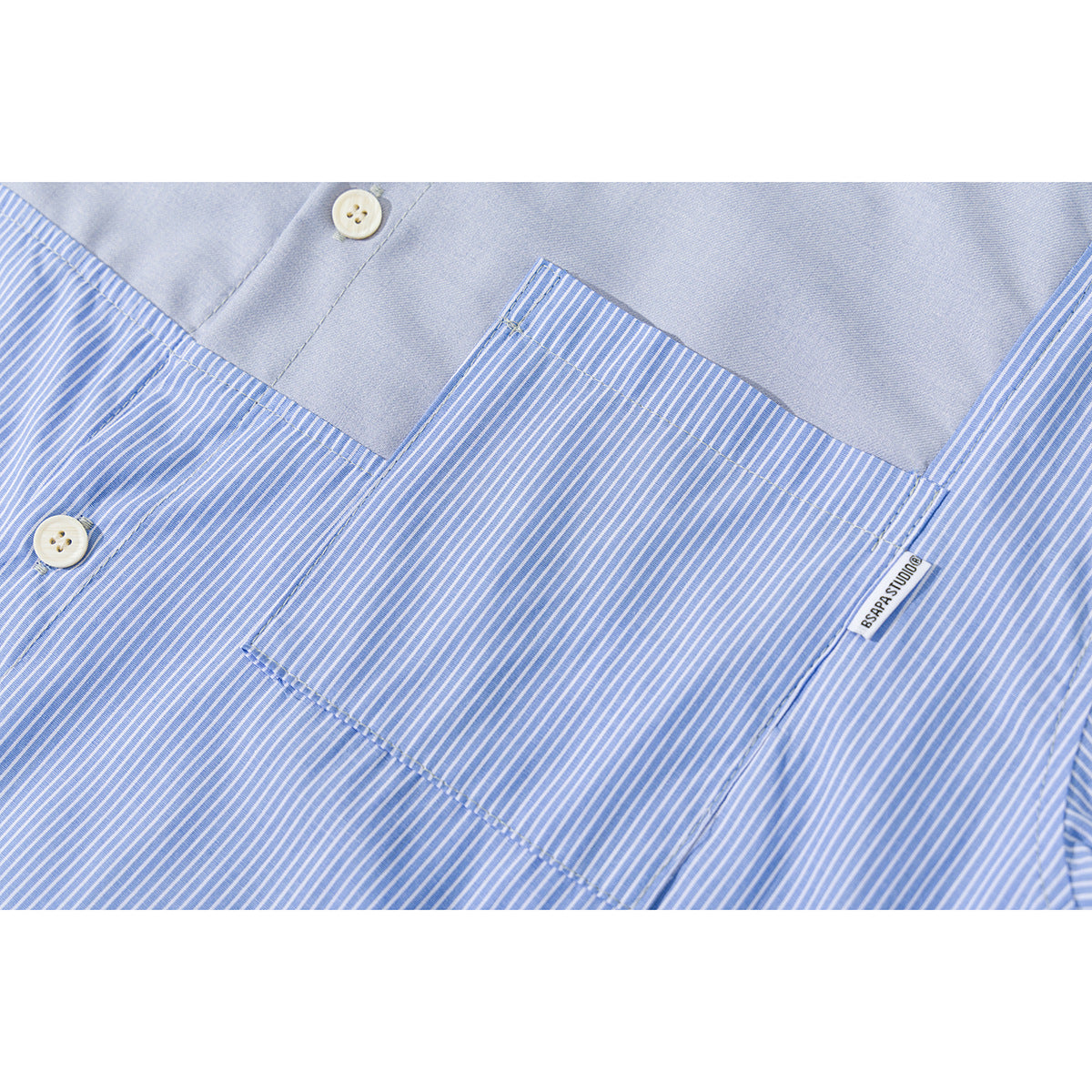 Close-up of a blue-and-white striped shirt showing its chest pocket, solid blue panel, buttons, and small sewn label.