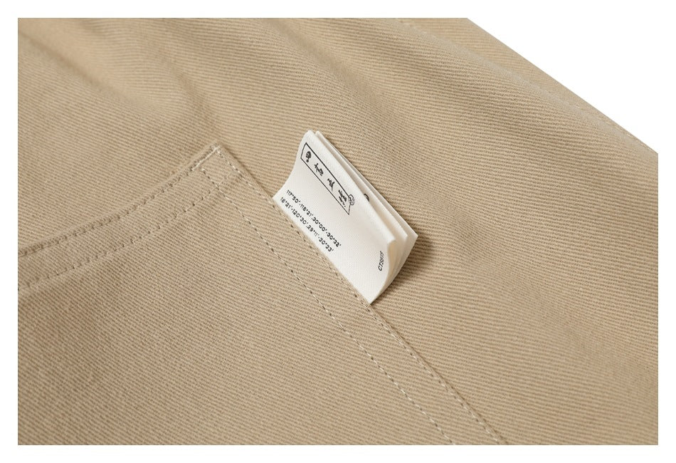 Close-up of a small care label tucked beside a stitched pocket on beige pants.