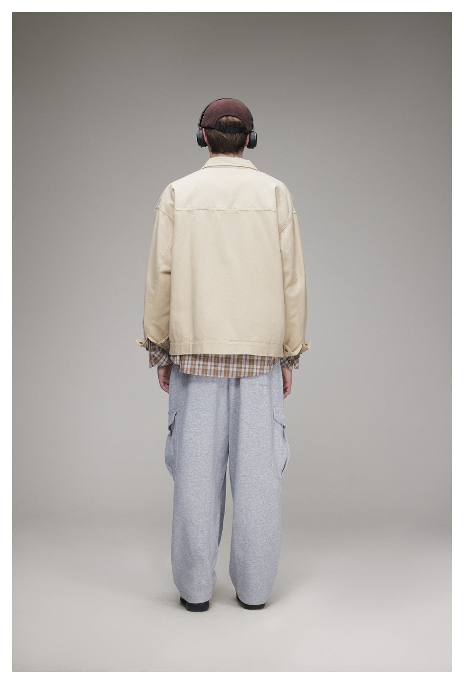 Back view of a model wearing a light beige jacket with a plaid shirt hem and loose gray cargo pants.