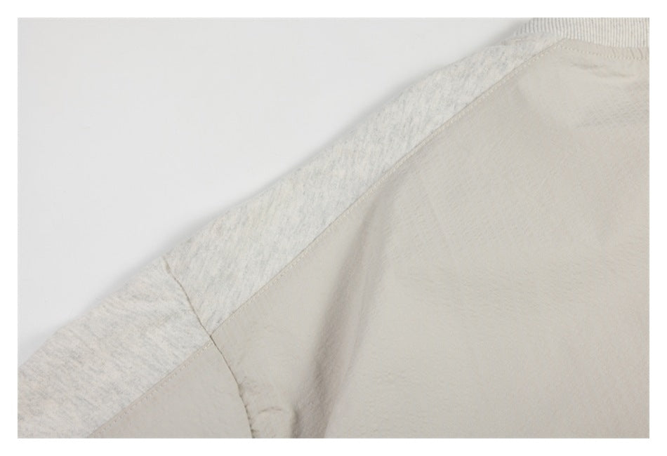 Close-up of a pale heather-gray garment's shoulder seam and contrasting light beige body panel.