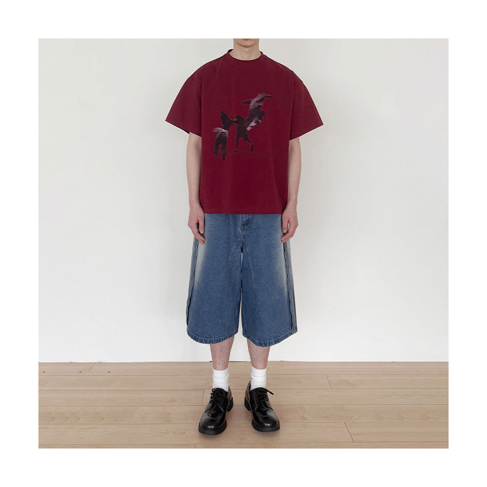 Model wearing a burgundy graphic T-shirt with loose blue denim shorts, white socks, and black shoes.