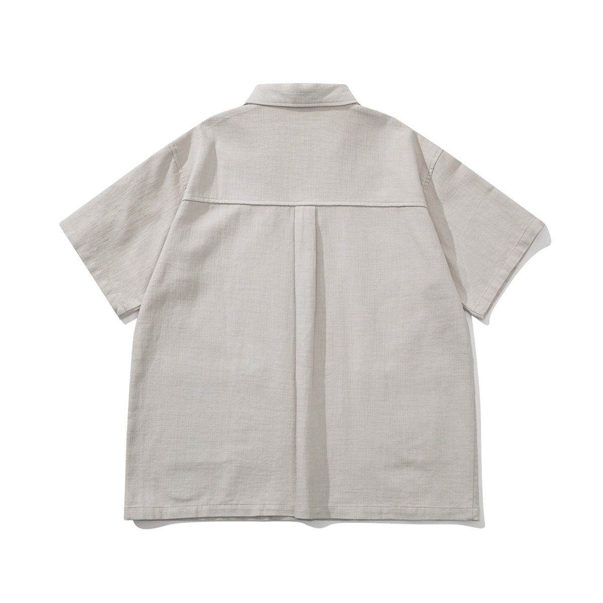Back view of a light beige short-sleeve shirt with a center pleat and a horizontal shoulder yoke.