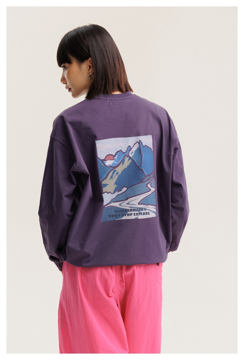 Closer rear view of a model wearing a plum T-shirt with a large colorful mountain print and loose bright pink pants.