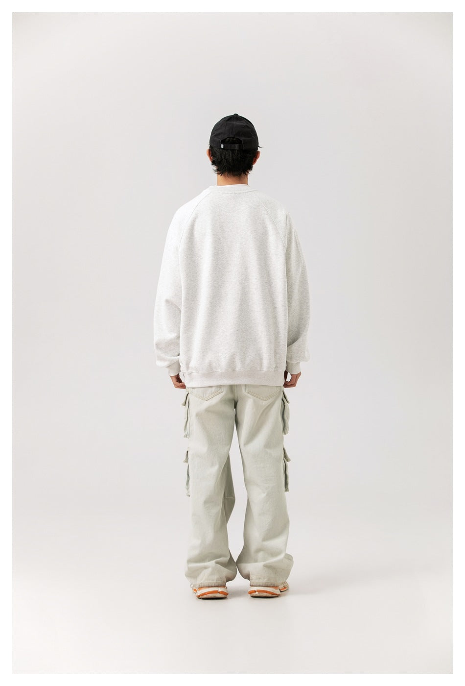 Full-length rear view of a model wearing a plain light gray sweatshirt and pale cargo pants.
