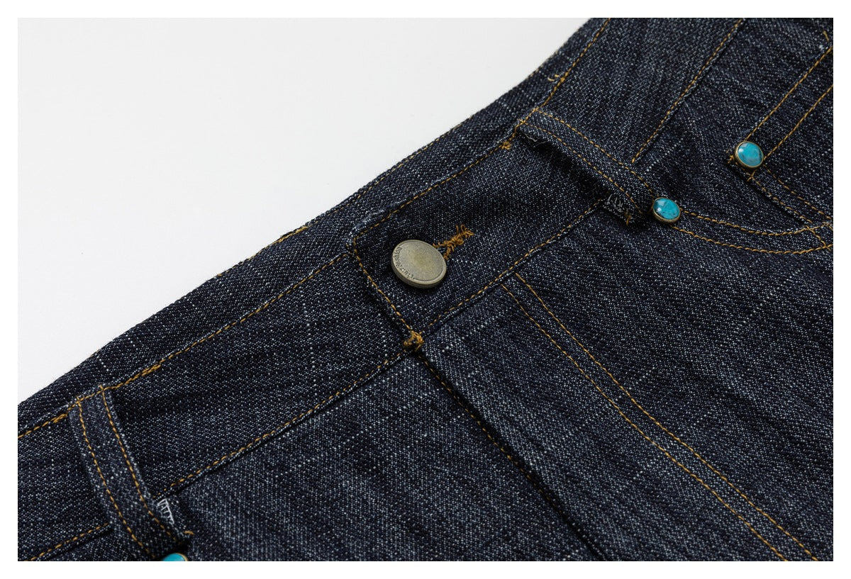 Close-up of the pants’ waistband and front closure, showing a metal button, turquoise rivets, and contrast stitching.