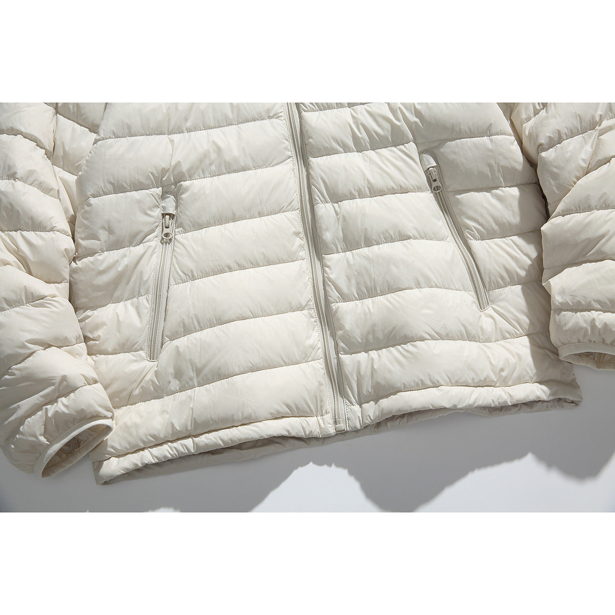 Close-up of an ivory quilted puffer jacket front with a central zipper and two zippered pockets.
