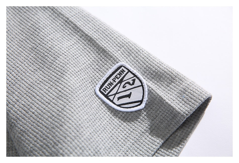 Close-up of a white shield-shaped embroidered patch on the gray textured sleeve.