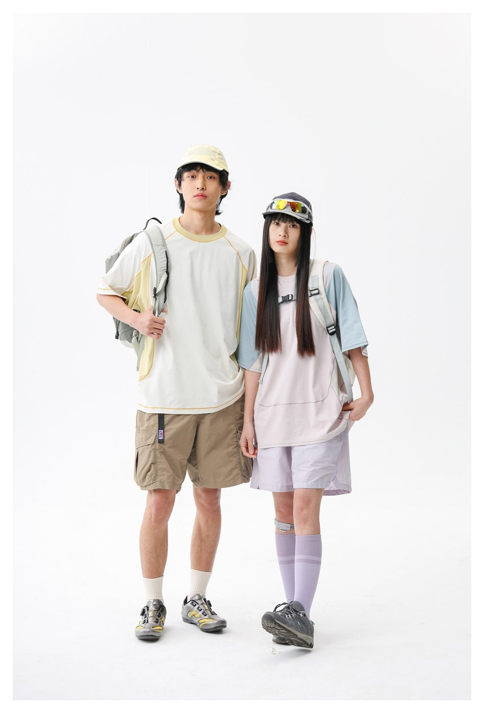 Two models pose together in color-block short-sleeve tops and outdoor shorts, wearing backpacks.