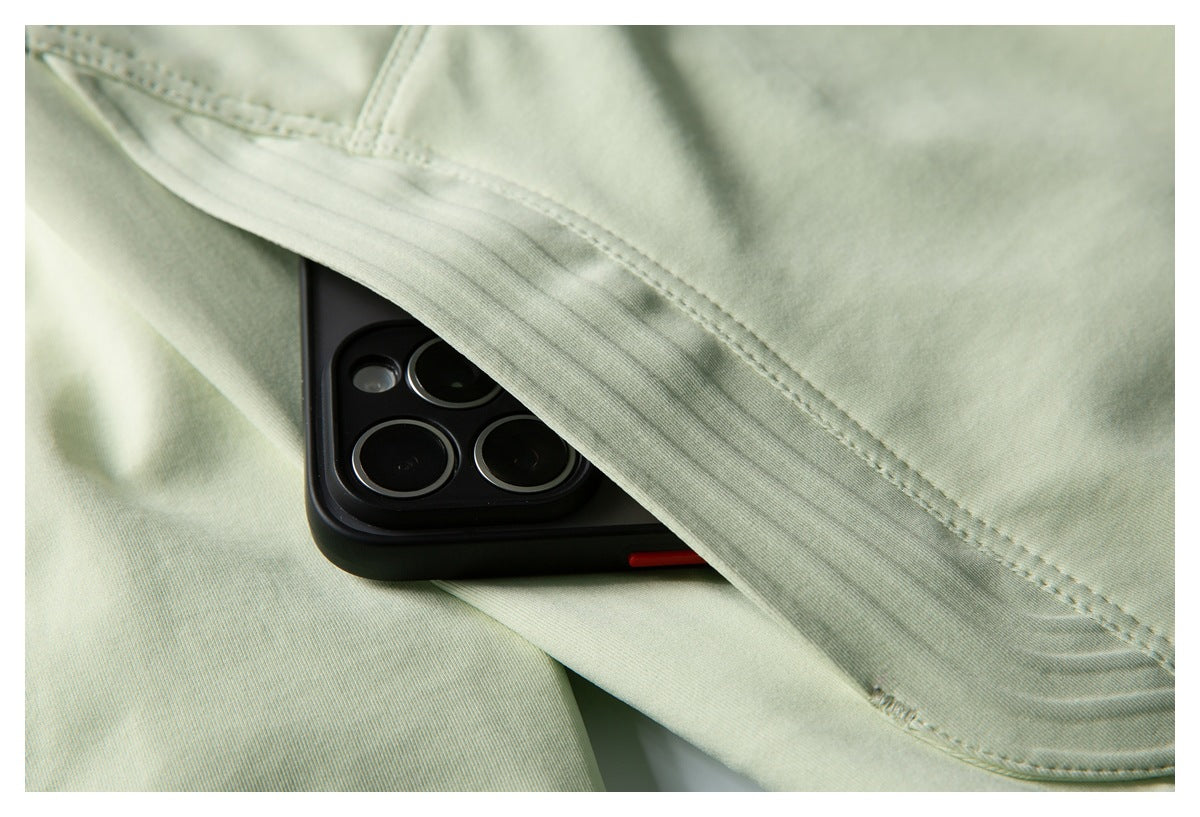 Close-up of pale sage-green jacket fabric and stitched pocket holding a black smartphone.