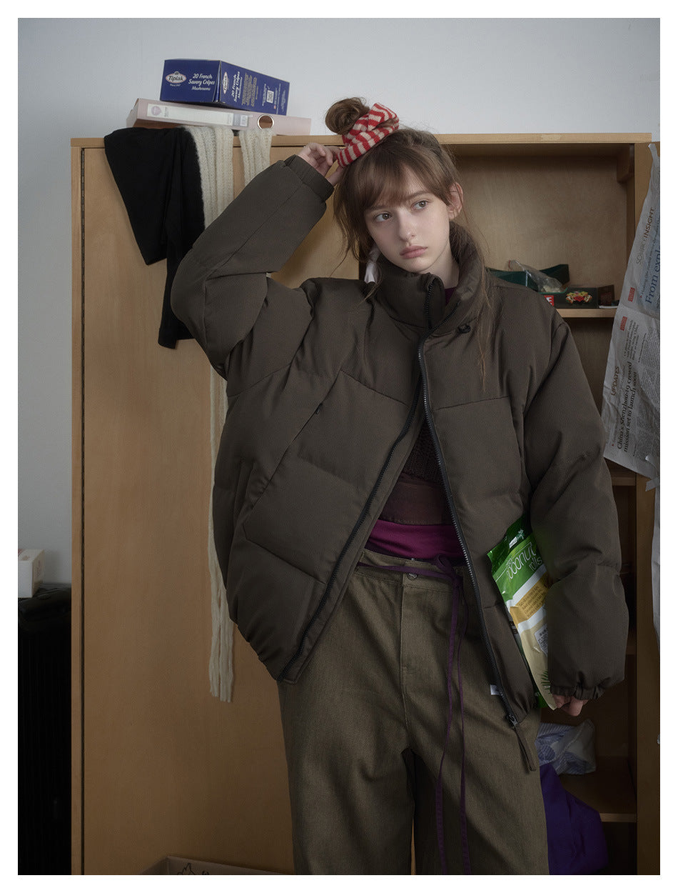 Model wearing a dark olive-brown puffer jacket with a high collar and front zipper, shown from the front.