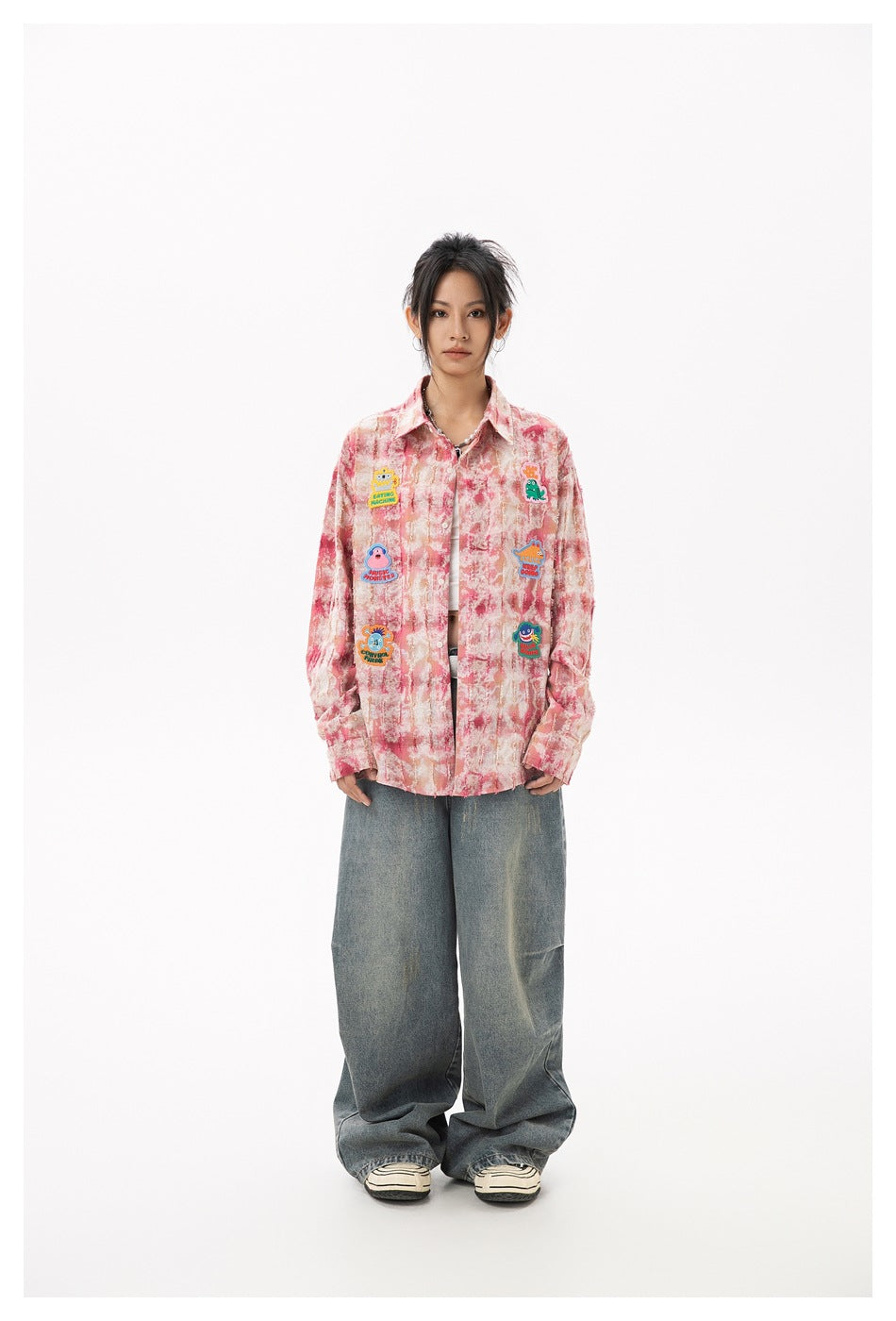 Full-length model wearing a pink marbled button-up shirt with colorful patches and wide-leg jeans.