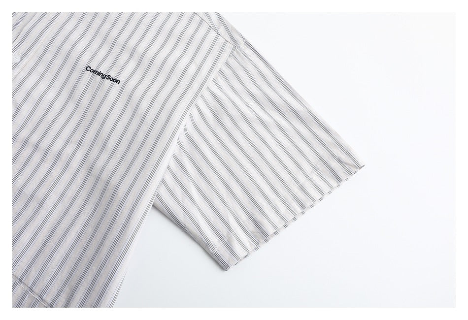 Partial flat-lay front of a white short-sleeve shirt with fine gray stripes and black chest embroidery.