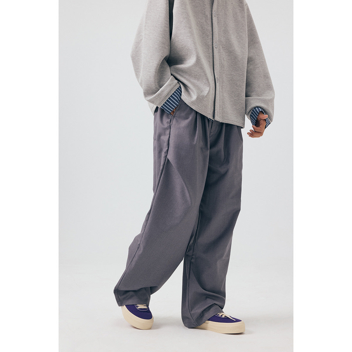 Cropped front view of a model wearing loose gray trousers with a gray button-front jacket and striped cuffs.