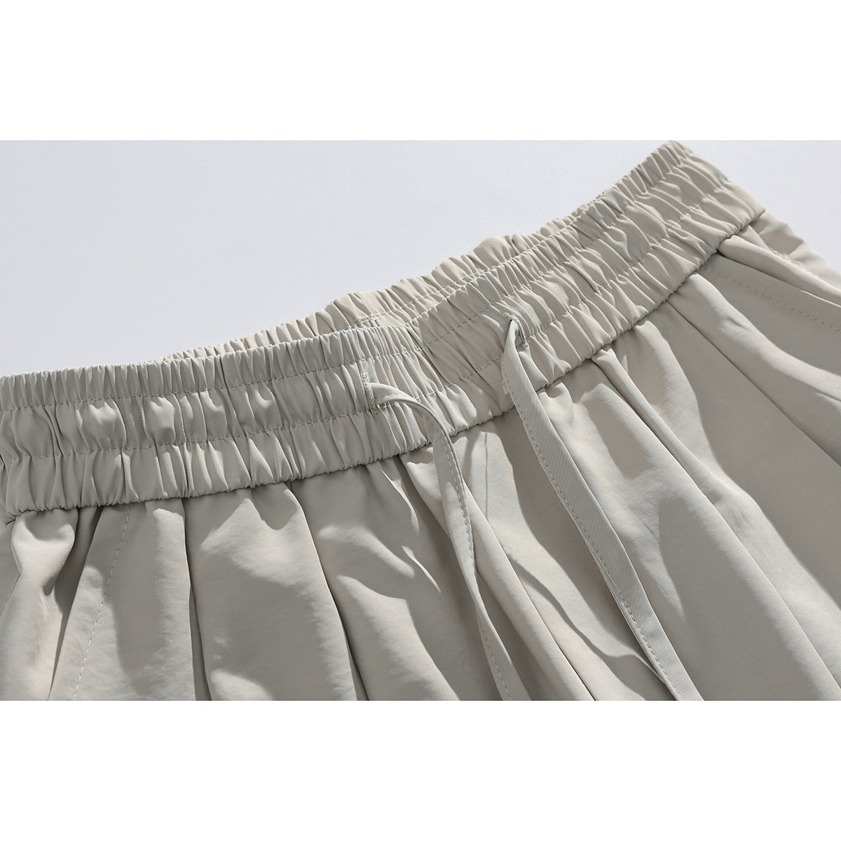 Close-up of light beige shorts showing the gathered elastic waistband, drawstrings, and pleated fabric.