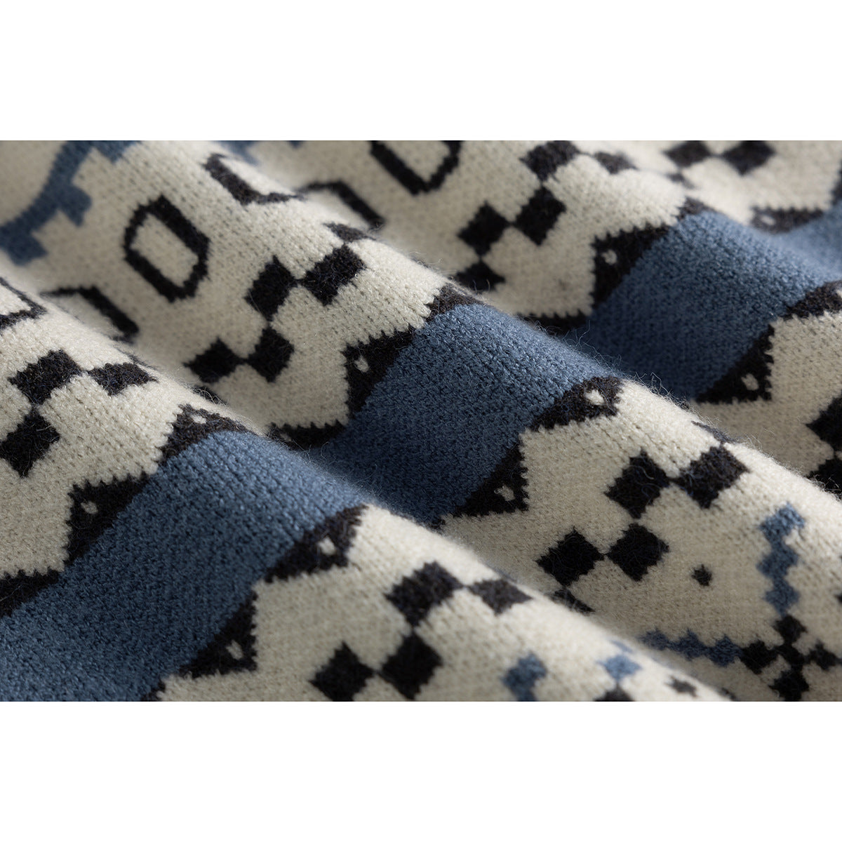 Close-up of ivory knit fabric with dark geometric motifs and broad blue bands, showing its textured pattern.
