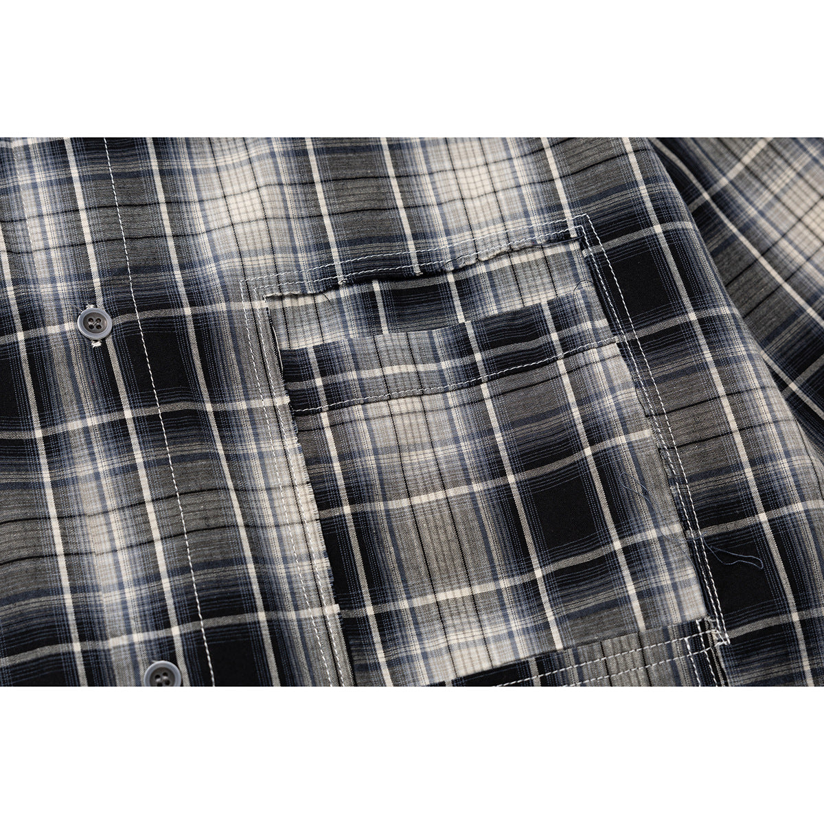 Close-up of a chest pocket and buttons on a black, gray, and cream plaid shirt.