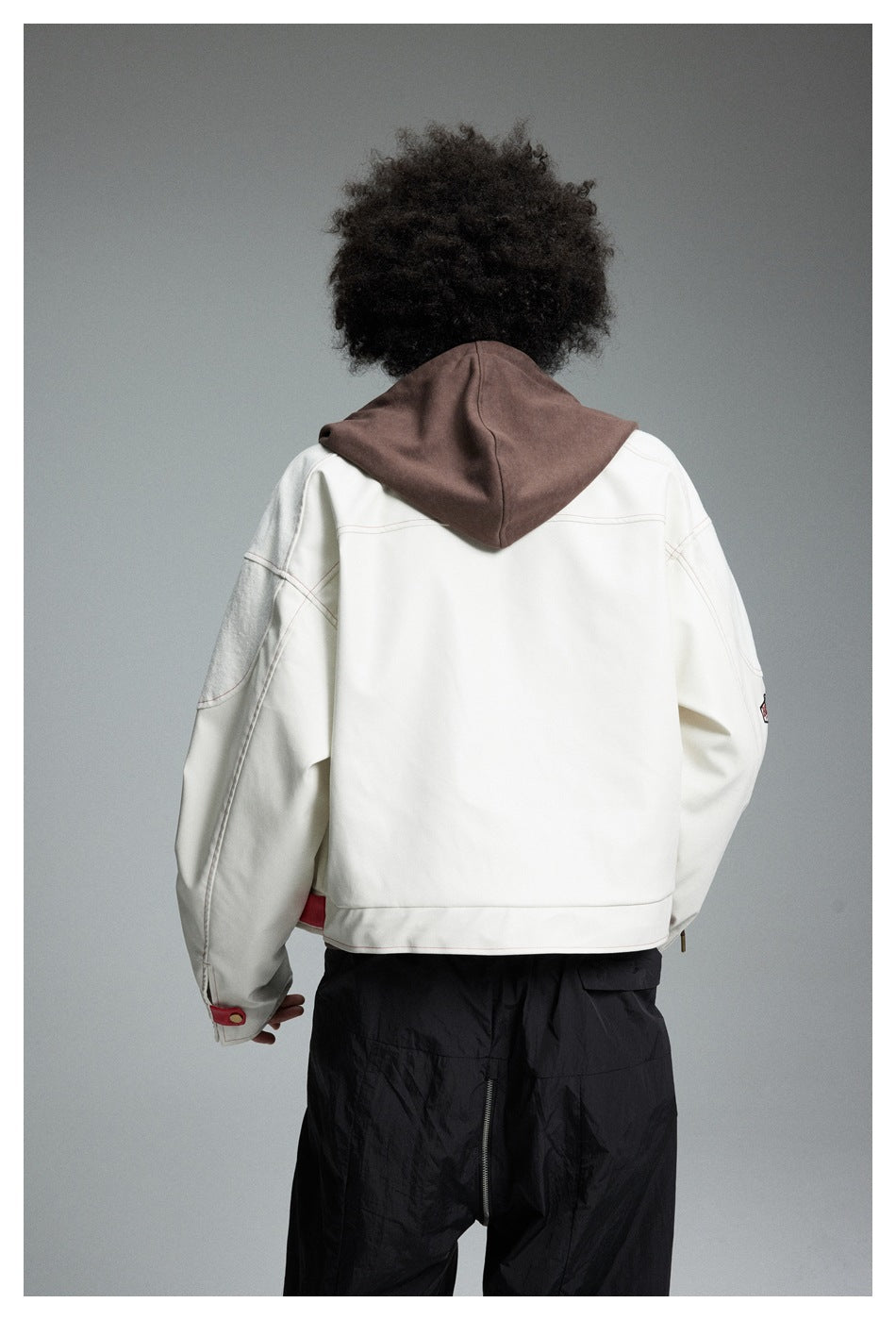 Rear view of a model wearing a cream jacket with a brown hood and red cuff and hem accents.