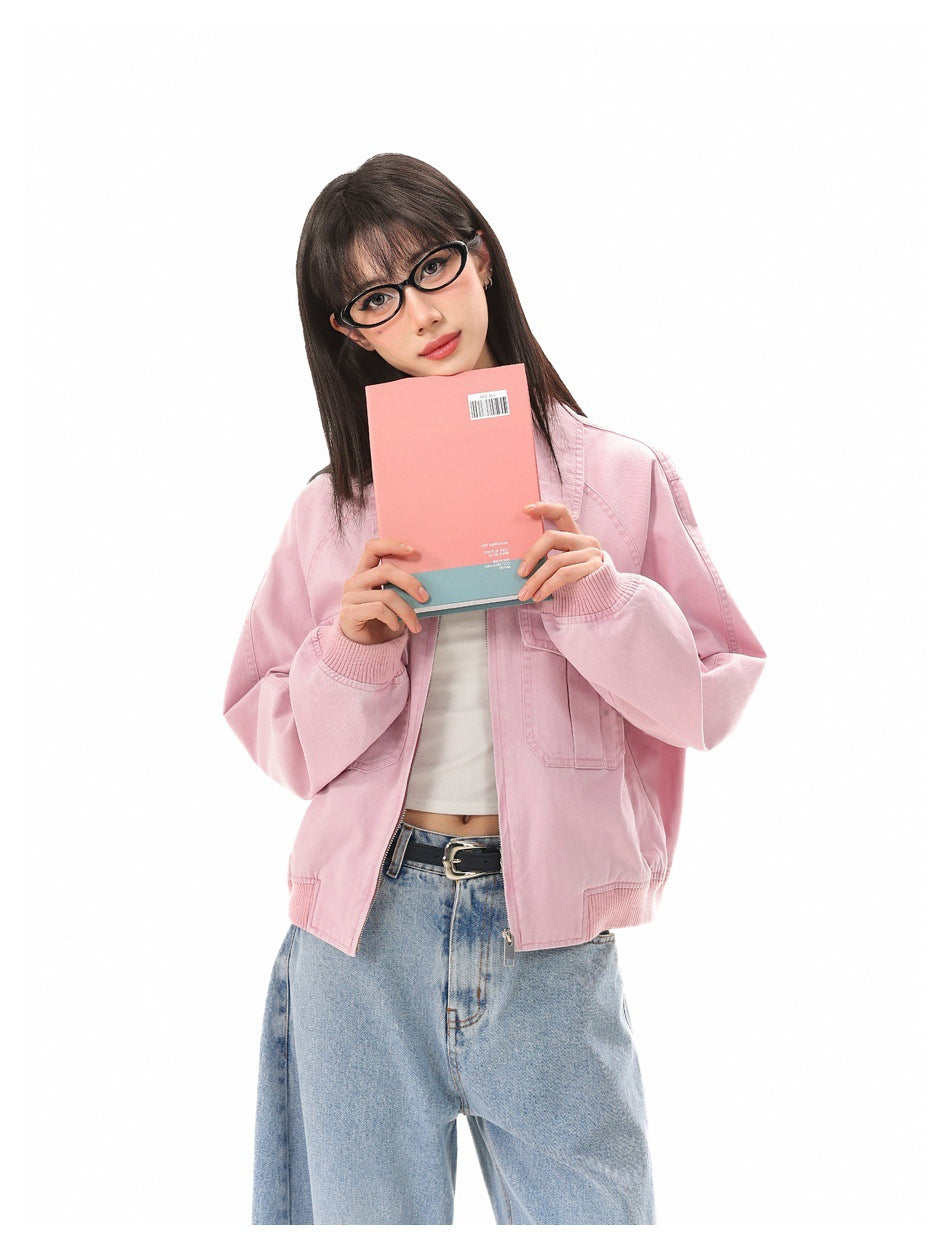 Model wearing a light pink zip-front jacket with flap chest pockets, holding a pink book in front of her.