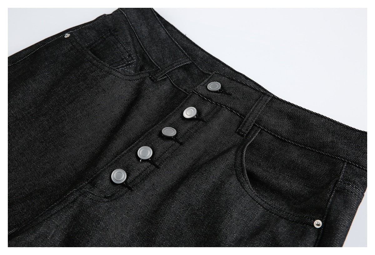 Close-up of black jeans showing the waistband, silver button fly, belt loop and curved front pocket.