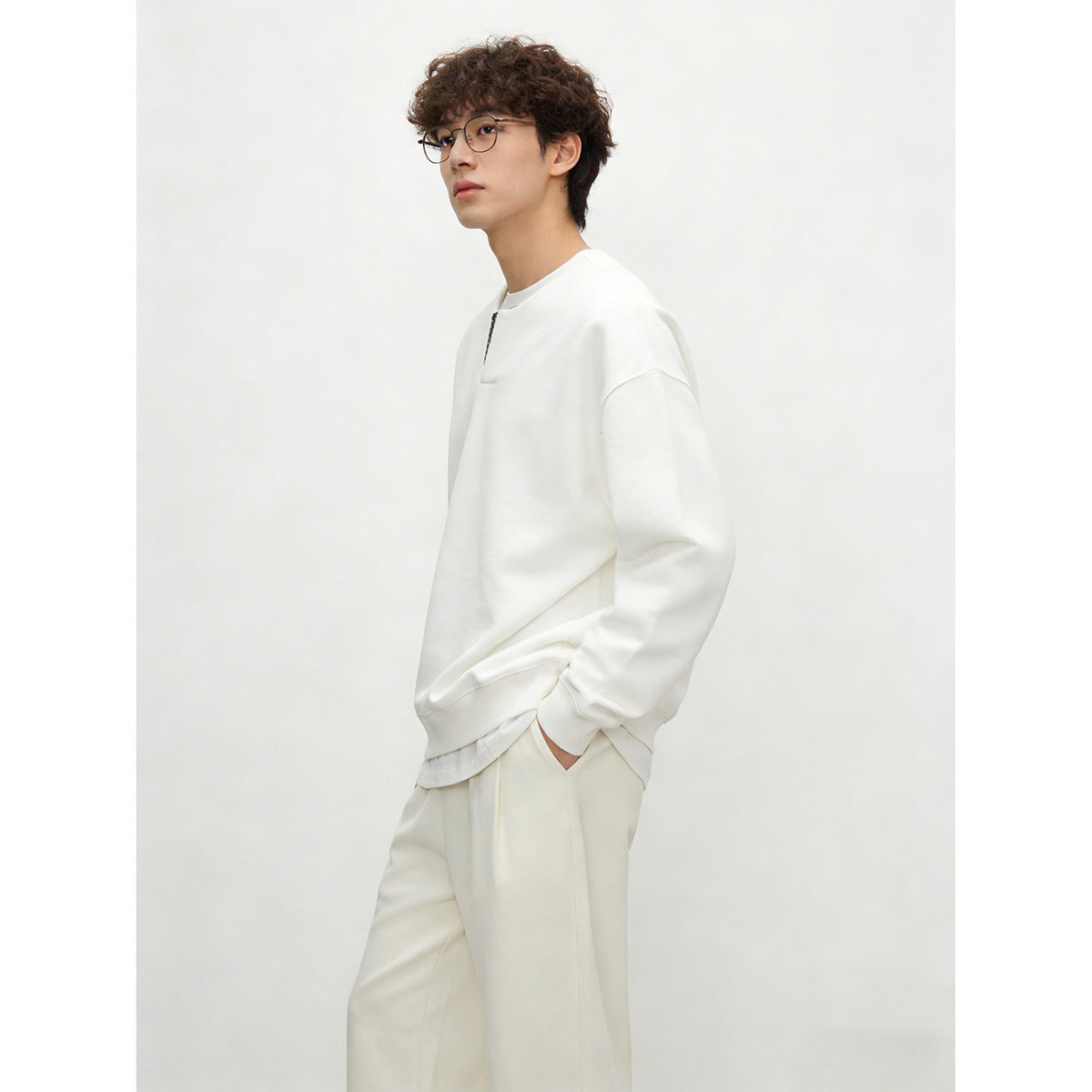 Three-quarter side view of a model wearing an ivory sweatshirt with a patterned neckline insert and matching pants.