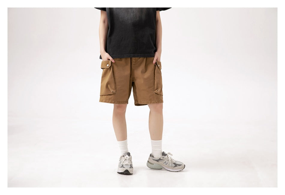 Front view of a model wearing brown cargo shorts with flap pockets, a black T-shirt, white socks and sneakers.