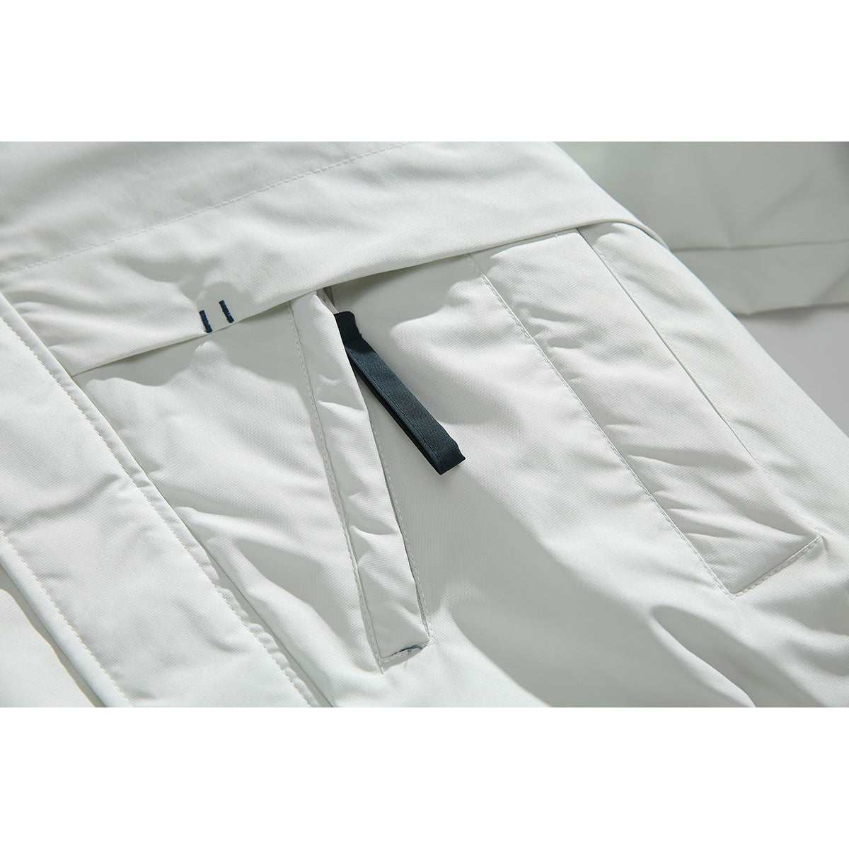 Close-up of a white jacket pocket with a black pull tab and small dark stitch accents.