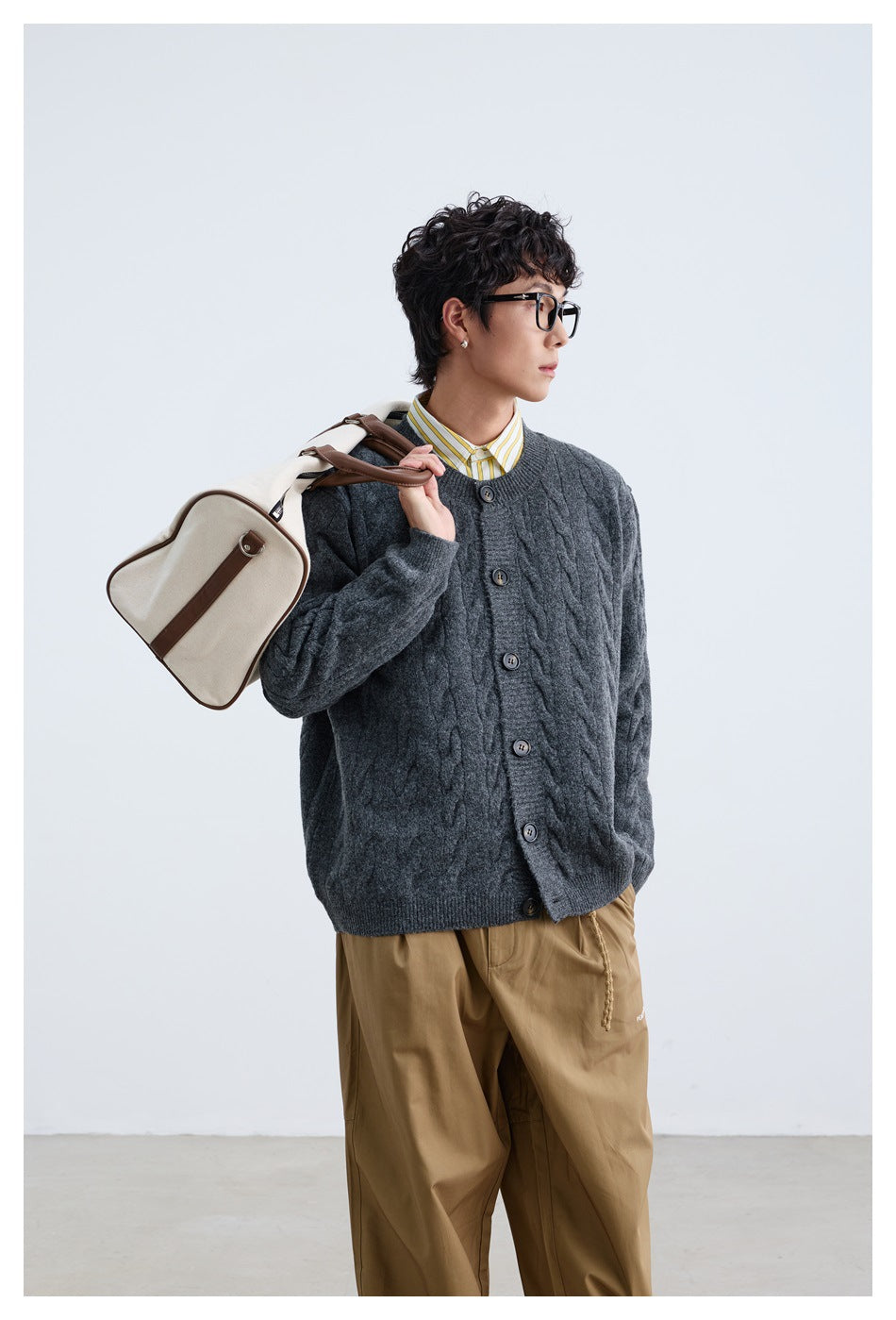 Three-quarter view of a model wearing a charcoal cable-knit button cardigan with tan trousers.