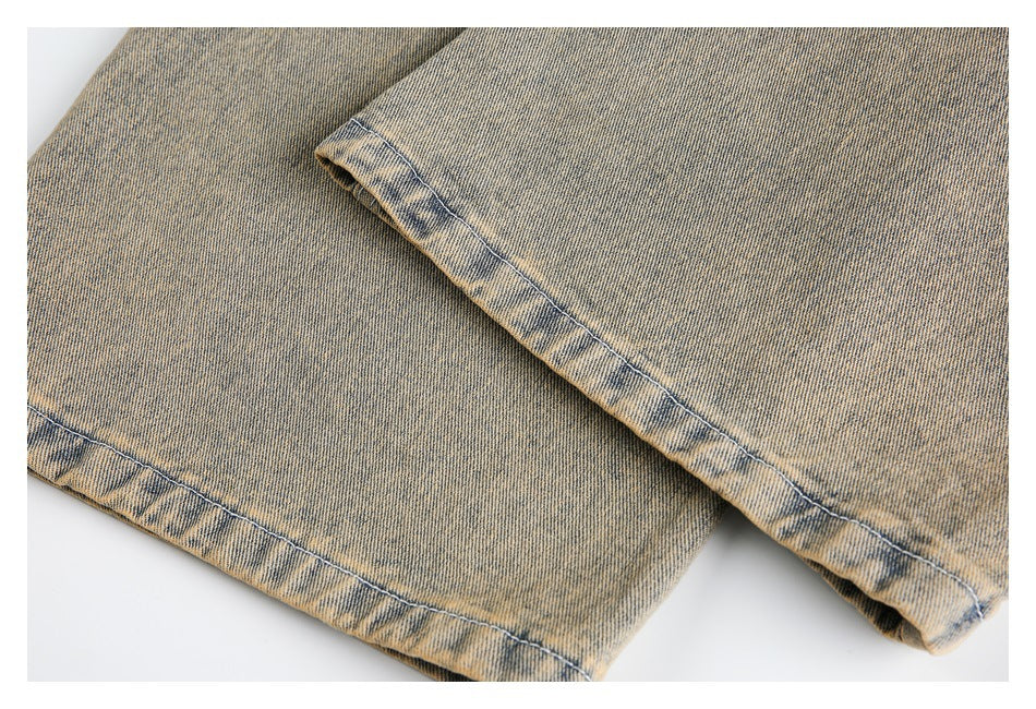 Close-up of the stitched hems on faded tan denim jeans.