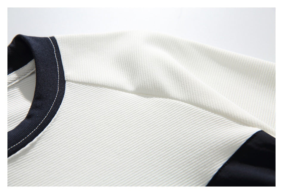 Close-up of the white ribbed shirt's shoulder seam, black-trimmed neckline, and black sleeve panel.