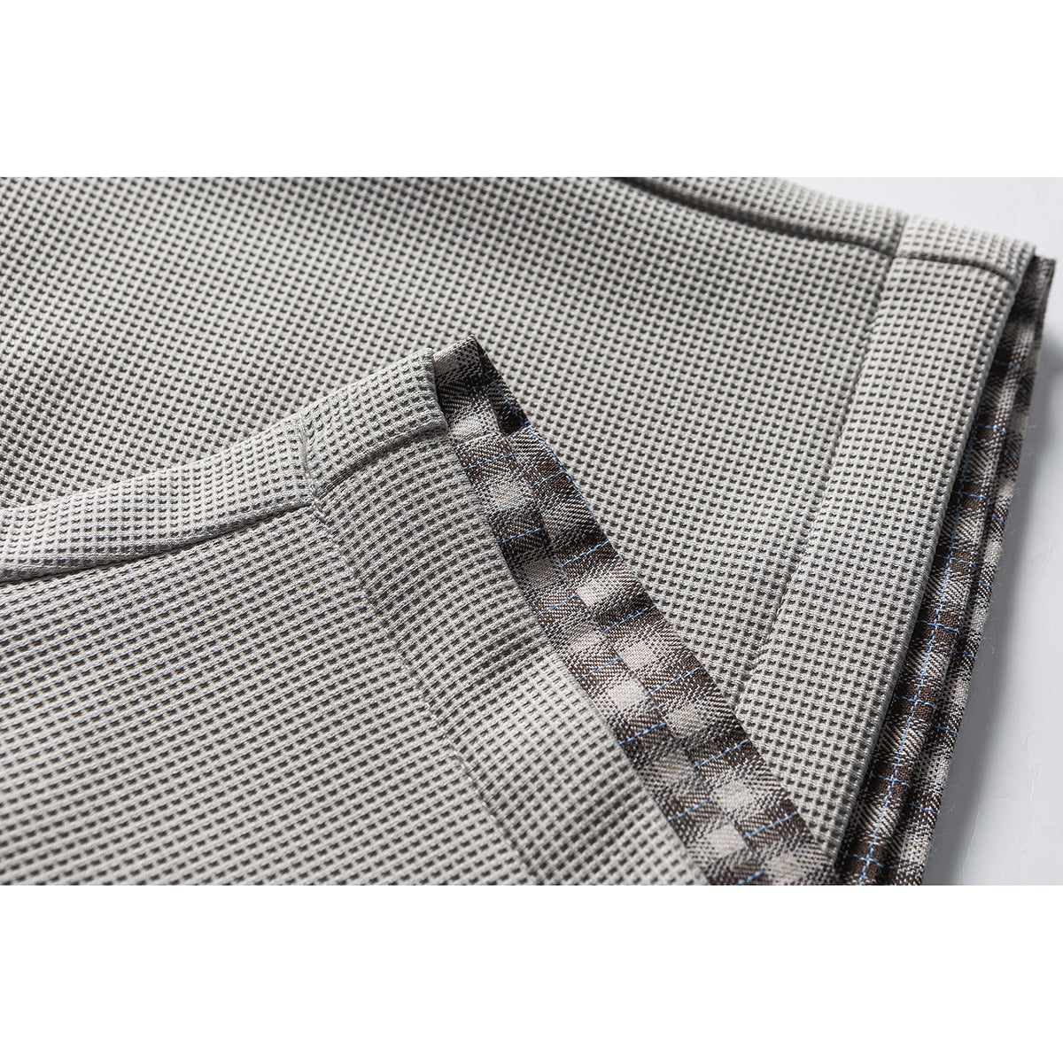 Close-up of light gray textured trousers showing a stitched seam and dark patterned inner trim.