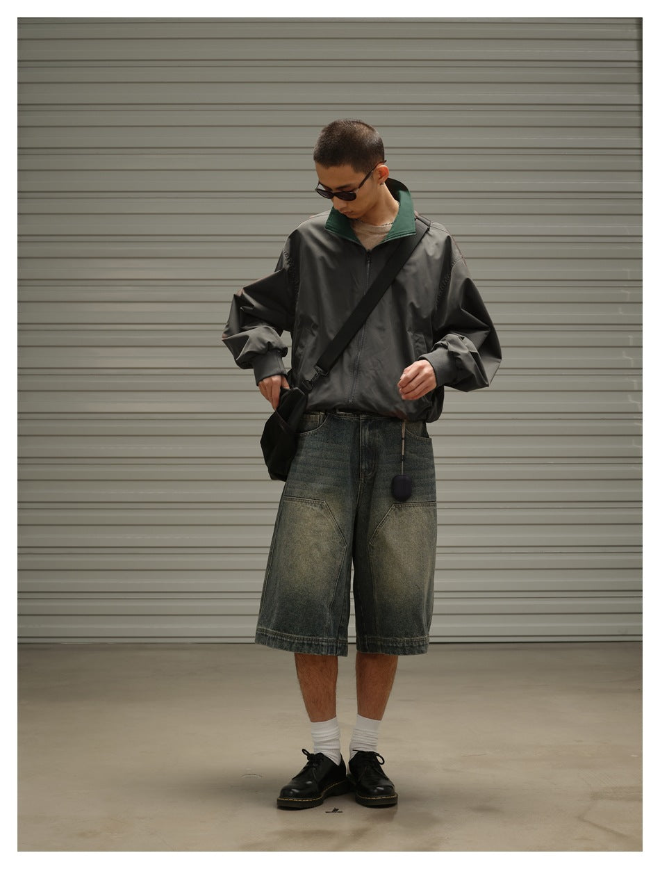 Model wearing a charcoal zip jacket with a dark green collar, black crossbody bag, and oversized faded denim shorts.