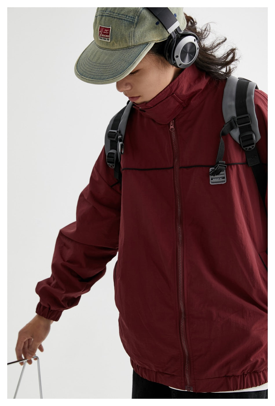 Close view of a model wearing a burgundy jacket, showing its high collar, front zipper, black chest piping and sleeve.